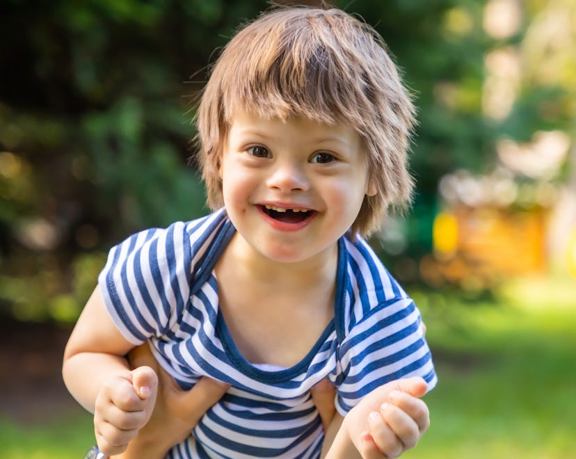 Portrait of Cute baby boy with Down syndrome playing in summer day on nature in article about spring...