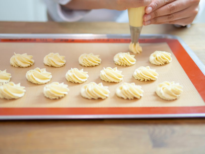 Hands piping butter cookies without eggs on baking tray in kitchen.