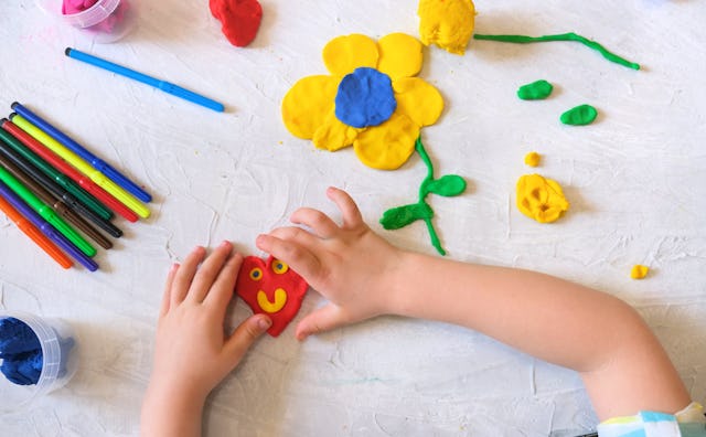 Hands of little girl making flower and sun and other  from colorful clay dough, plasticine, Home Edu...