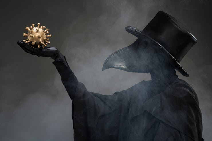 The plague doctor holds a golden model of the virus in his hand.
