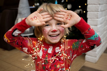 smiling cheerful child in a festive make-up of a deer, numbers of new year 2023 are written on palms...