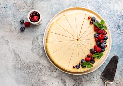Classic New York cheesecake with fresh berries on light blue concrete background, top view