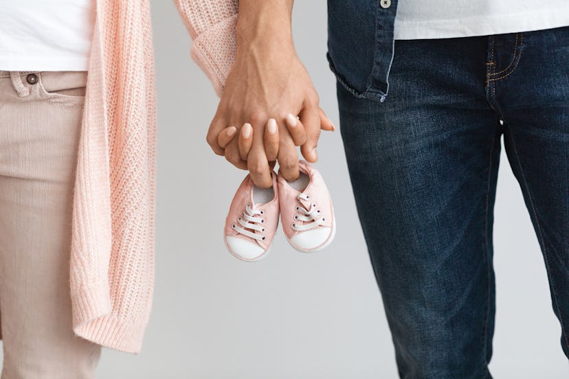 Closeup of pregnant couple carrying small baby shoes while holding hands: valentines day pregnancy a...