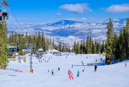 Beautiful view of Colorado ski resort on clear winter day; people skiing and snowboarding to base of...