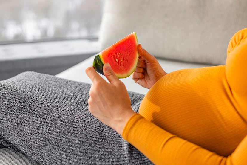 Pregnant woman eating watermelon slice during summer pregnancy. Some moms swear by fruit to fight na...