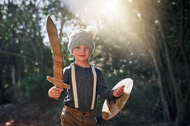Portrait of an adorable little boy playing with a cardboard sword and shield outside. Xander is a gr...
