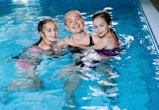 Mother with two daughters having fun in indoor swimming-pool. Girl is resting at the water park. Swi...