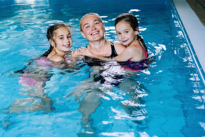 Mother with two daughters having fun in indoor swimming-pool. Girl is resting at the water park. Swi...