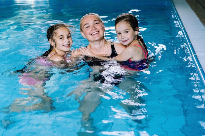 Mother with two daughters having fun in indoor swimming-pool. Girl is resting at the water park. Swi...