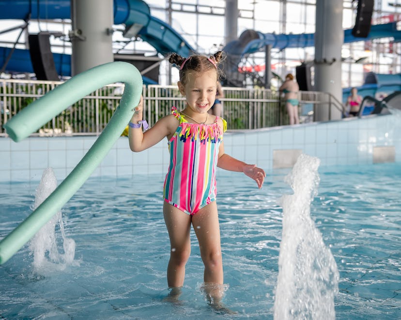 little beautiful girl playing with a foam noodle in a indoor pool. rest in the water park