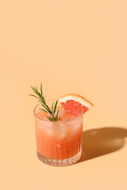 Grapefruit juice garnish rosemary sprig on color beige background. Mocktail Paloma. Close up. Vertic...