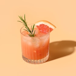 Grapefruit juice garnish rosemary sprig on color beige background. Mocktail Paloma. Close up. Vertic...