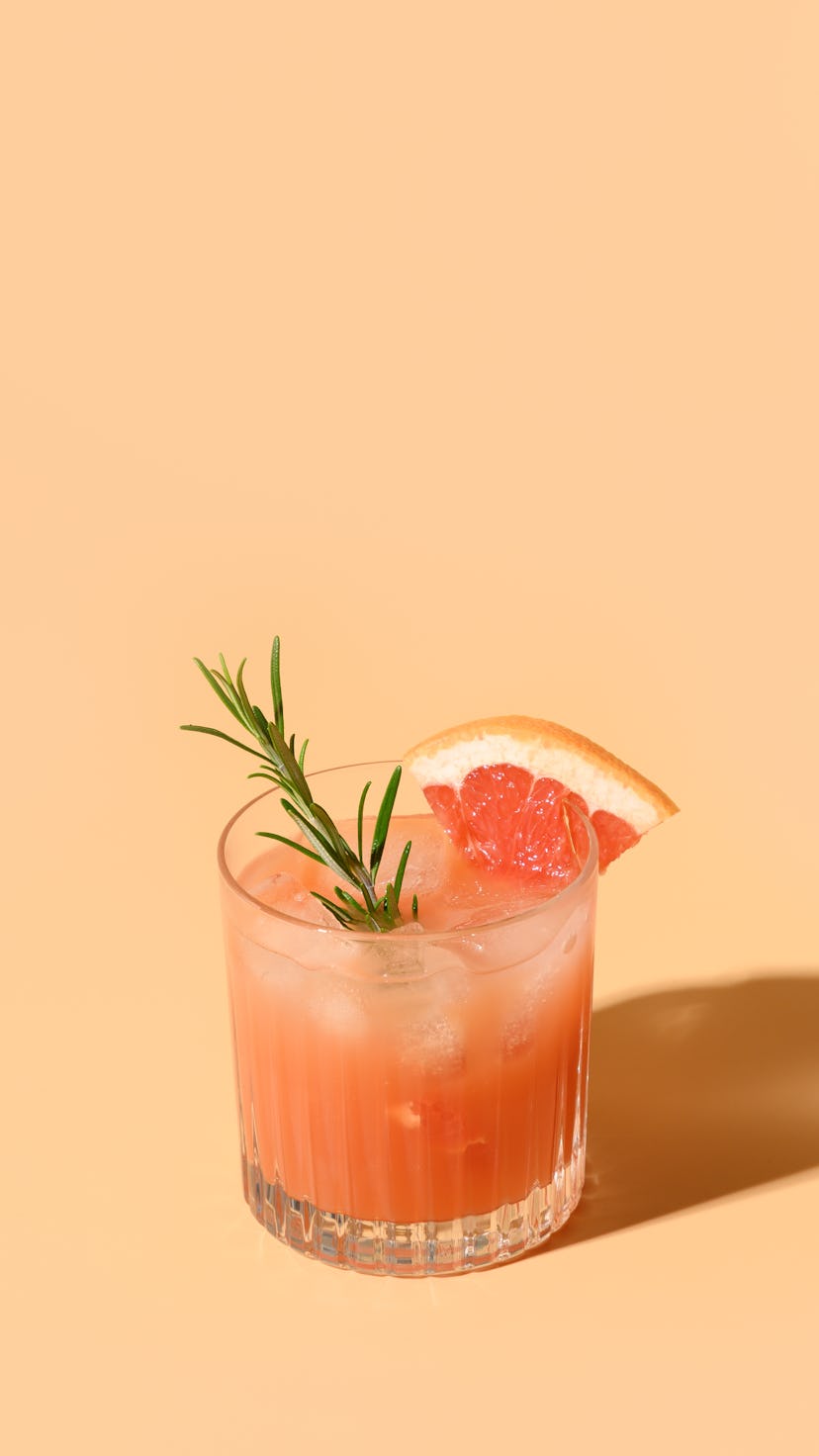 Grapefruit juice garnish rosemary sprig on color beige background. Mocktail Paloma. Close up. Vertic...