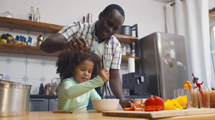 Happy african father and daughter making dough for pizza having fun together in kitchen indoors. Por...