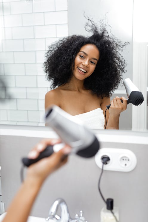 Shot of a young woman blowdrying her hair in the bathroom