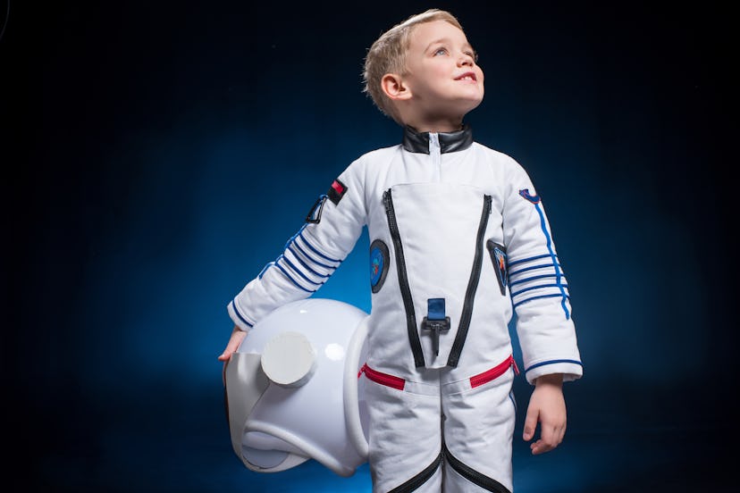 Cute little boy in space suit holding helmet and looking at distance. Celestial names for boys are a...