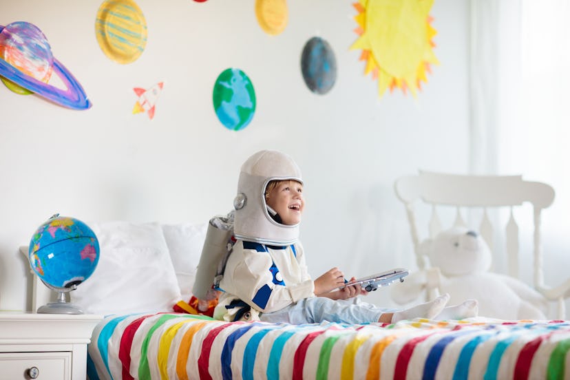 Kids play astronaut. Little boy in space costume jumping on bed with rocket. Celestial names for boy...