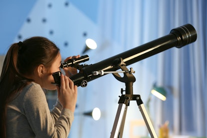 Cute little girl with telescope looking at stars in evening, perhaps finding some celestial names fo...