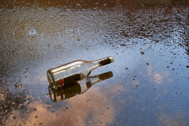Alcoholism problem concept. Empty bottle of liquor on a wet floor after rain at sunset