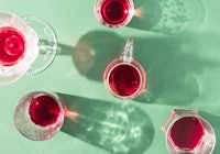 Glasses of red drinks with sunlit shadows on green background. Creative summer party concept.  Flat ...