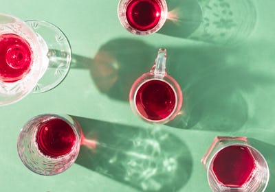 Glasses of red drinks with sunlit shadows on green background. Creative summer party concept.  Flat ...