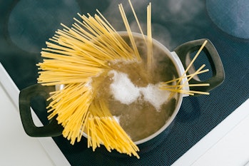 Spaghetti in pot is cooked in boiling water on electric ceramic hob. Top view, soft focus, yellow gl...