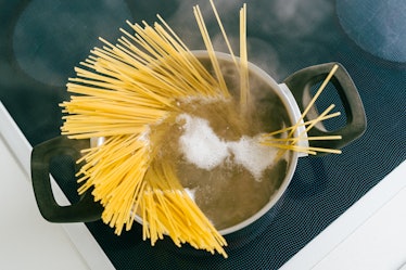 Spaghetti in pot is cooked in boiling water on electric ceramic hob. Top view, soft focus, yellow gl...