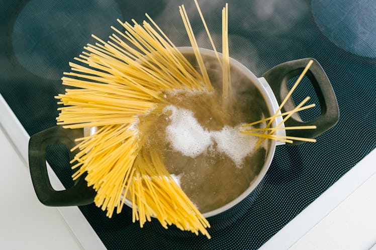 Spaghetti in pot is cooked in boiling water on electric ceramic hob. Top view, soft focus, yellow gl...