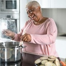 Happy senior woman having fun preparing lunch in modern kitchen - Hispanic Mother cooking for the fa...