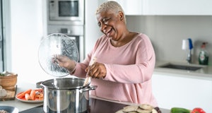 Happy senior woman having fun preparing lunch in modern kitchen - Hispanic Mother cooking for the fa...