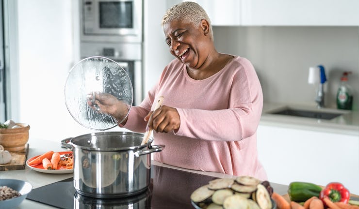 Happy senior woman having fun preparing lunch in modern kitchen - Hispanic Mother cooking for the fa...
