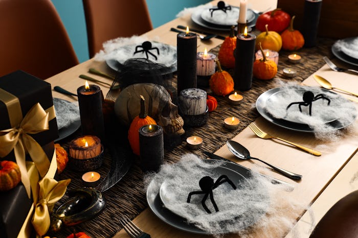 Festive table setting for Halloween party with burning candles, pumpkins, spiders and web