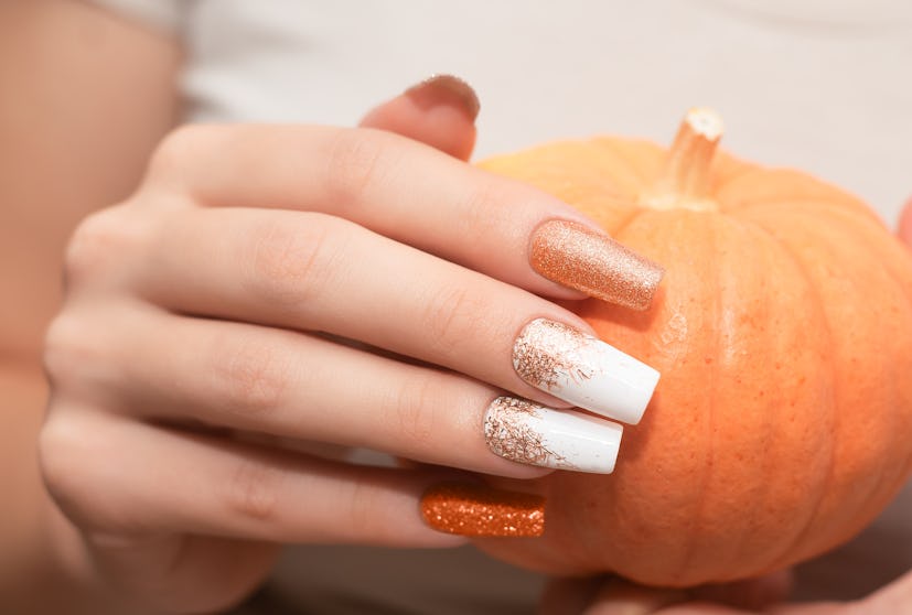 Female hand with long nail design. Glitter orange and white nail polish manicure. Female hand with p...