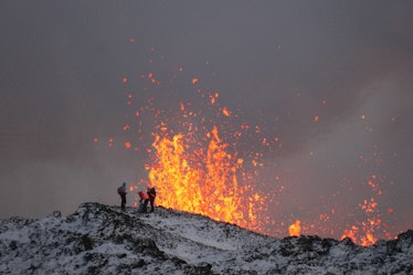 A team of scientists works on the ridge of a volcanic fissure as lava spews during a volcanic erupti...