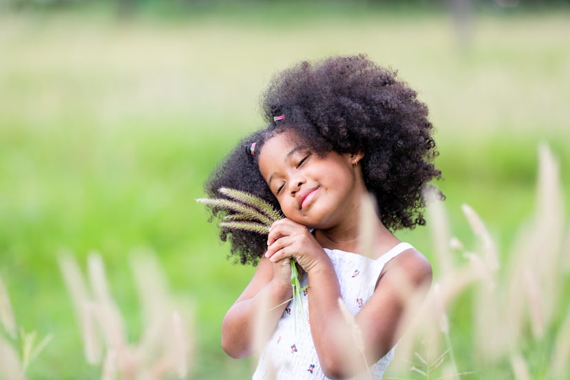 Little African American curly-haired girl in meadow with flowers in hand. Strong girl names include ...