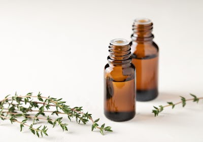 Thyme essential oil in a glass bottle close-up on a light background. Thyme branches are on the tabl...