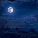 Mountain Road through the forest on a full moon night. Scenic night landscape of dark blue sky with ...
