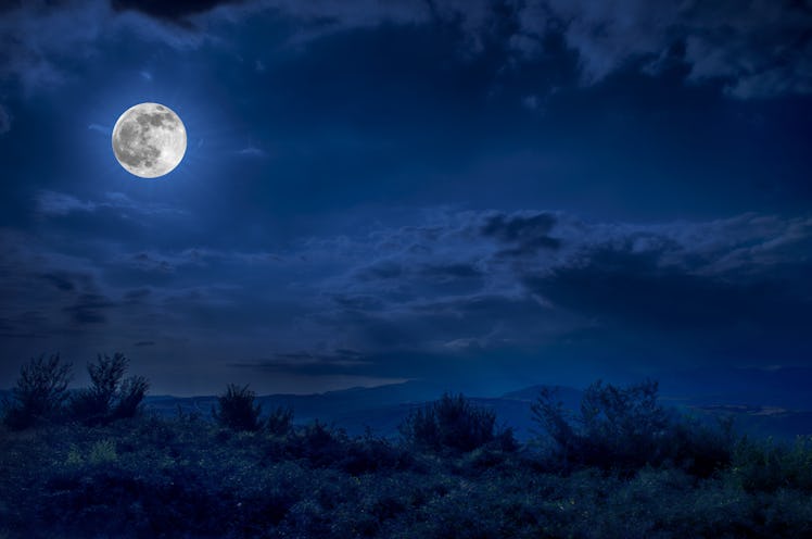 Mountain Road through the forest on a full moon night. Scenic night landscape of dark blue sky with ...