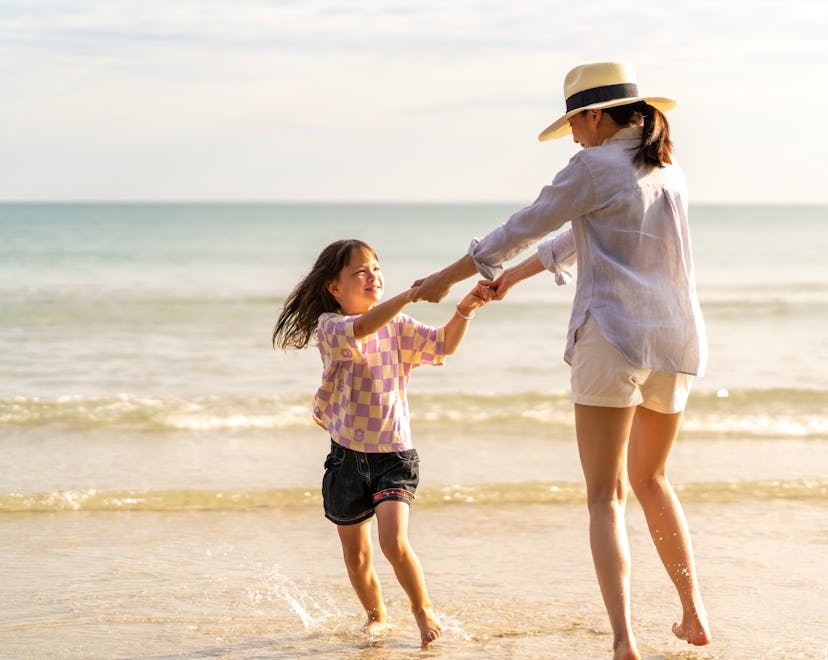 Happy Asian family on beach vacation. Mother and little daughter walking and playing together on tro...