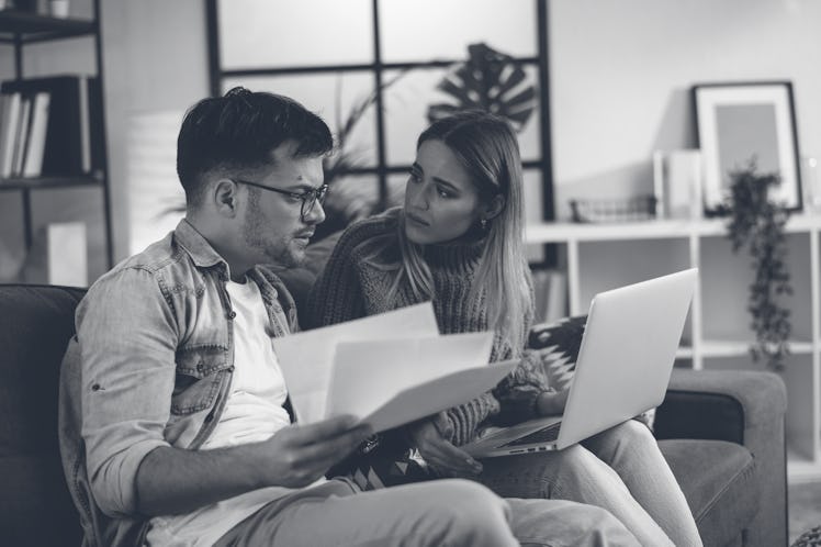 Worried couple paying their bills online with laptop at home in the living room. Couple having finan...