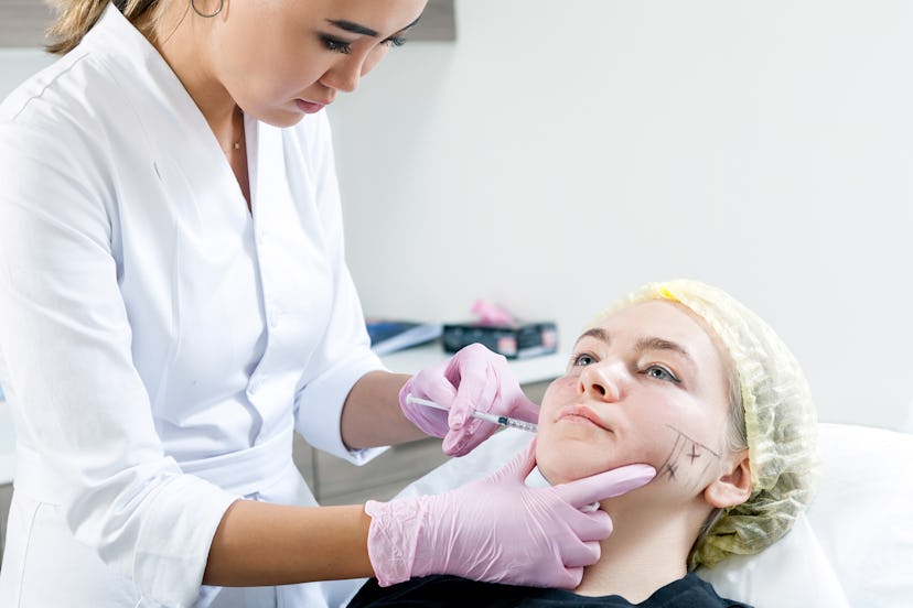 Close-up Young woman azitka doctor cosmetician in white lab coat and sterile gloves injects injectio...