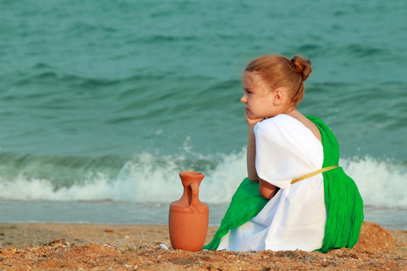 A little girl in a toga and tunic sits on the beach. Some 4 letter girl names are inspired by mythol...