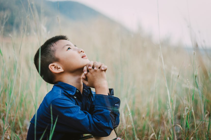 Little asian boy praying in a field. Many 4 letter boy names have religious meanings.