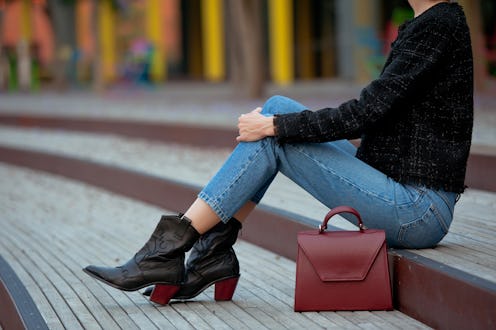 Fashionable young woman in high heel black cowboy boots, blue jeans, black tweed jacket and burgundy...