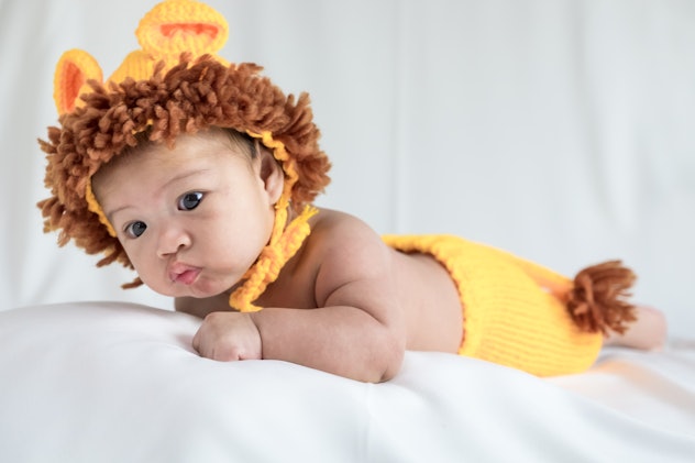 Baby in lion costume lying down on a white blanket. "Leon" is a good March baby name since it means ...