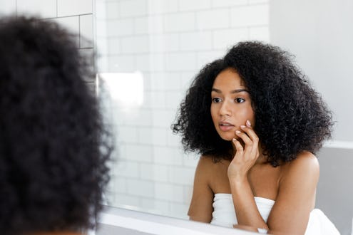 woman inspecting her skin in front of a bathroom mirror