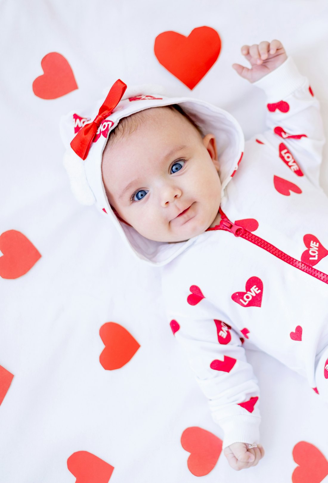 funny baby girl with red hearts on a bed on a white cotton bed smiling for a baby Valentine's Day ph...