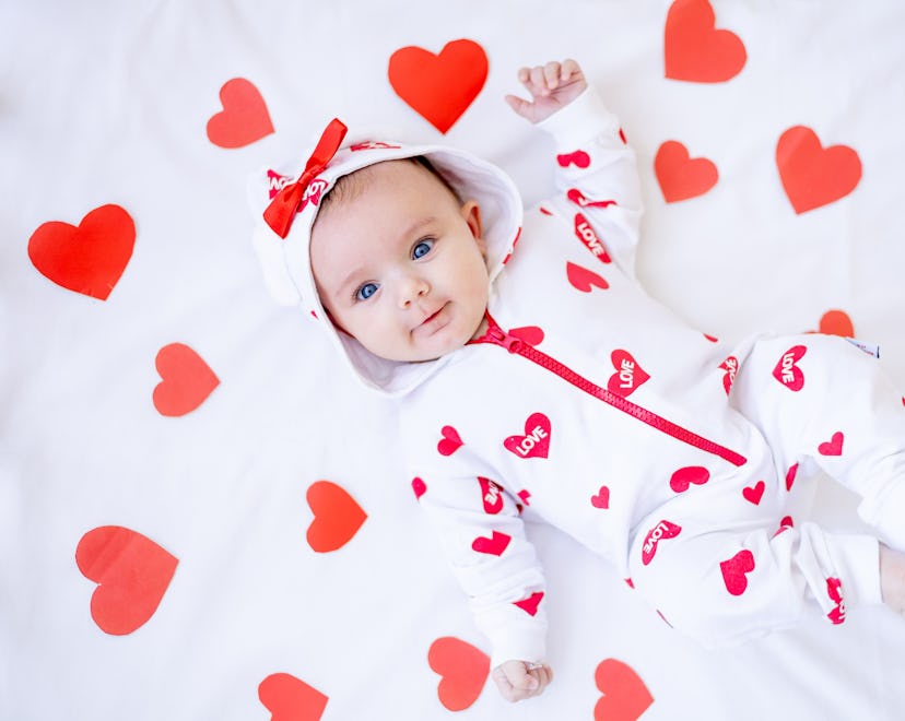 funny baby girl with red hearts on a bed on a white cotton bed smiling for a baby Valentine's Day ph...