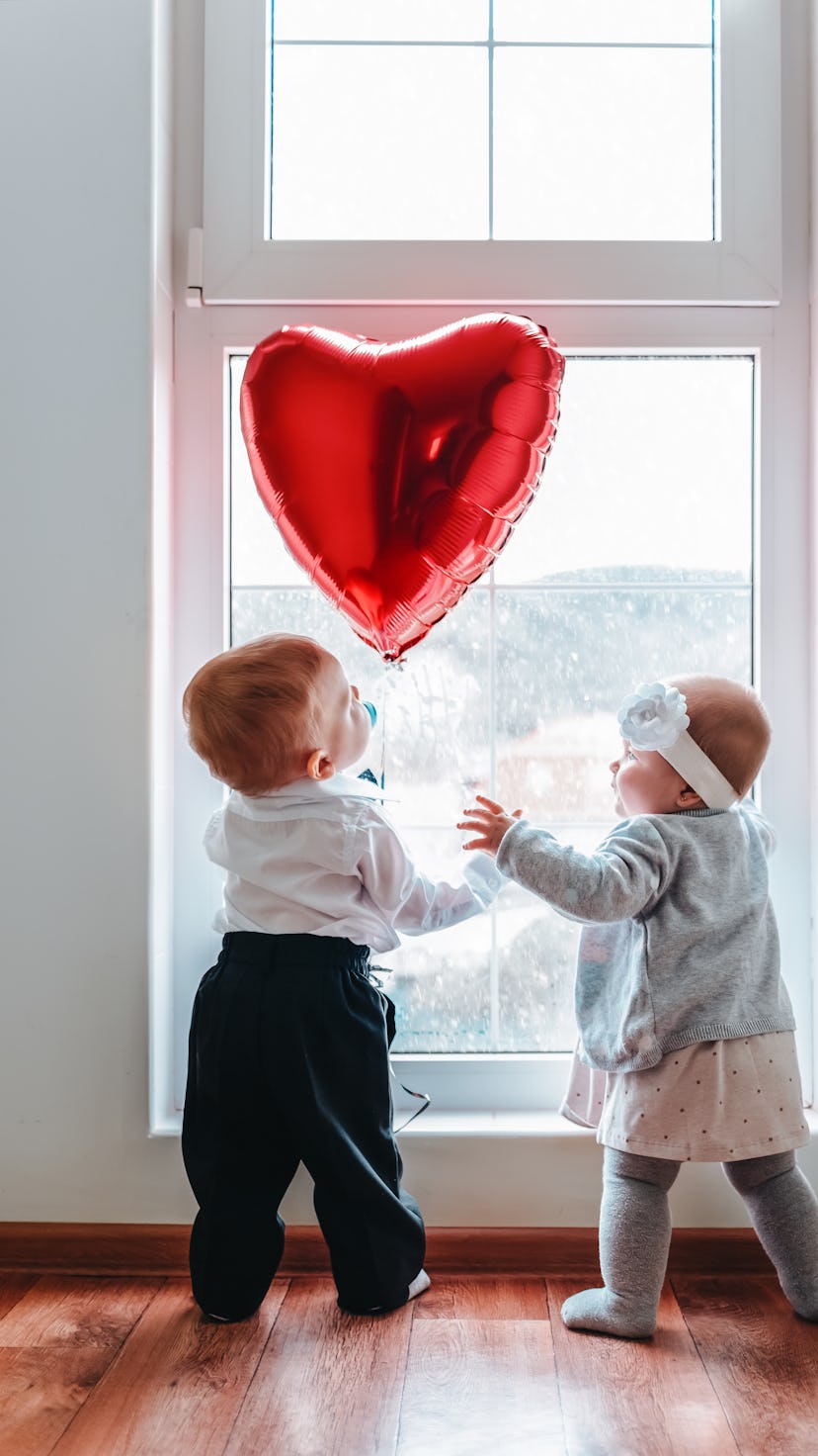 Cute baby boy and baby girl looking at the red heart balloon for Valentine's Day photoshoot.