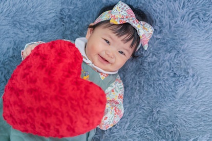 Asian baby valentine with red heart smiling and laying on carpet. 